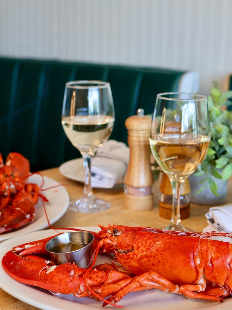 Two whole cooked lobsters with drawn butter and white wine on a restaurant table.