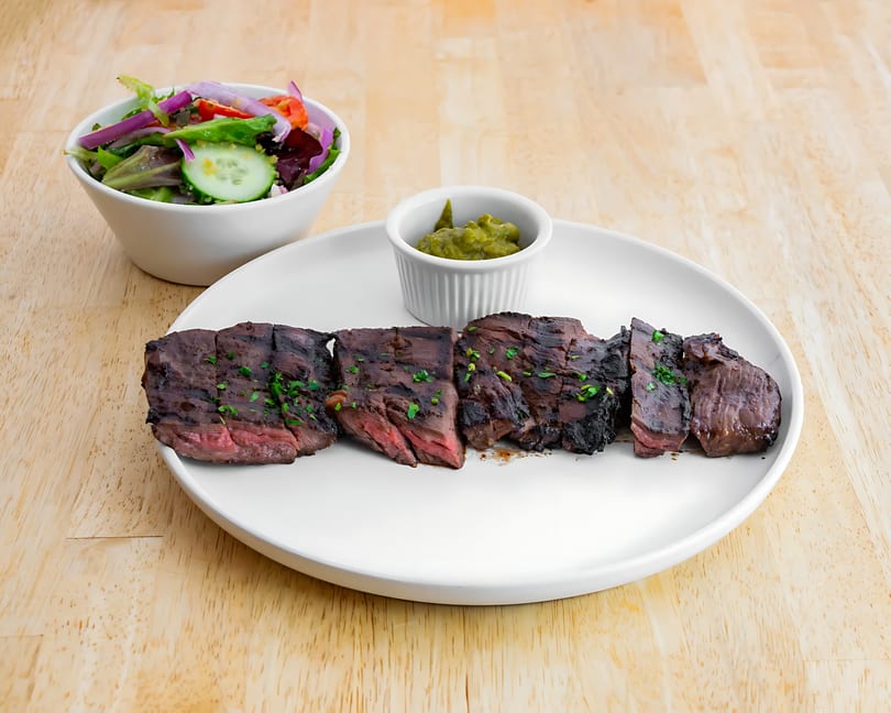 Grilled steak slices with a side salad and guacamole on a white plate.