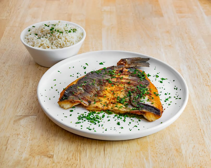 Grilled fish fillet with crispy skin and parsley, served with a side of white rice.